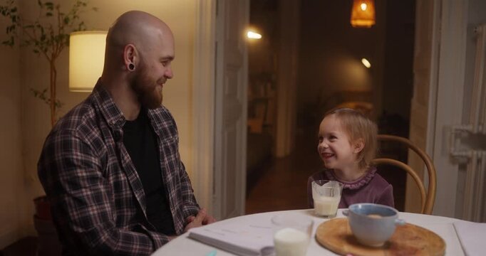 Smiles light up a cozy kitchen as a father and daughter share milk and snacks, creating beautiful memories together