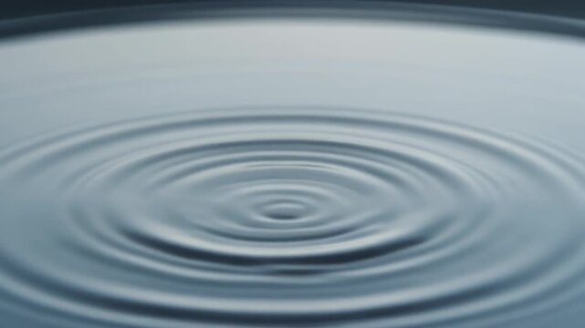 Close-up of water drop hitting surface creating ripples, slow motion