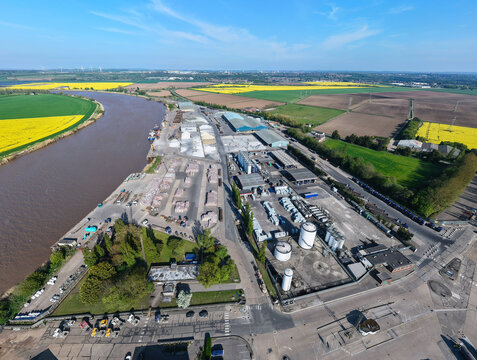 Aerial view of PD Ports industrial facility with warehouses and storage tanks along the River Trent near yellow rapeseed fields in Scunthorpe, England, United Kingdom.