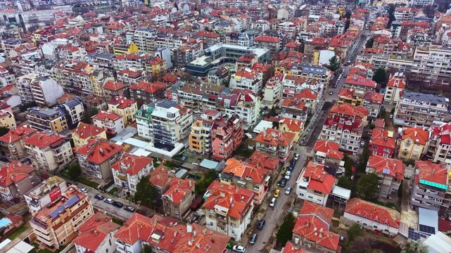 Many houses with red roofs fill the view of a residential area. Streets line the houses creating an organized grid. Buildings of various sizes dot the landscape under clear skies.