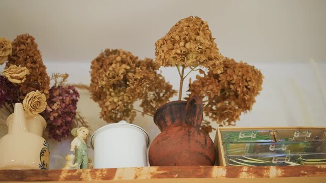 Dried hydrangea vase on kitchen shelf, rustic pottery and porcelain canister beside vintage trinket, warm light and soft shadows create nostalgic still tableau, preserved floral decor with earthy
