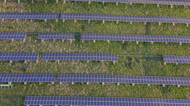 Aerial drone footage showing a top-down view of a small solar panel farm, featuring geometric rows of photovoltaic panels generating renewable energy