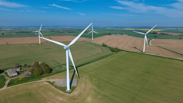 Aerial view of modern wind turbines standing in vast agricultural fields under a clear blue sky Eastoft, England, United Kingdom.