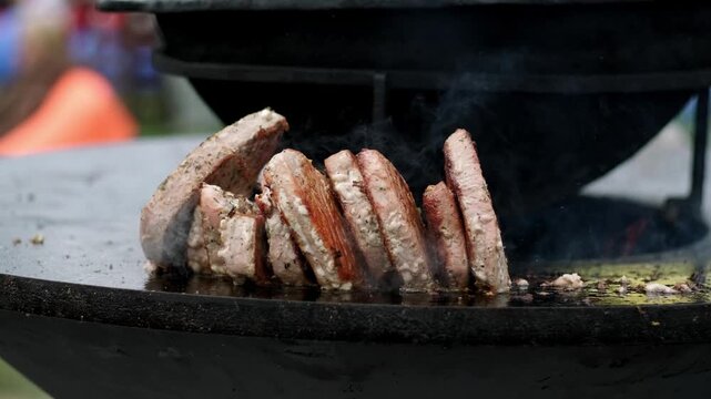 Meat patties grilling on a round metal hot plate. Cook preparing food outdoors over fire. Culinary process of searing beef cutlets for lunch or dinner barbecue.