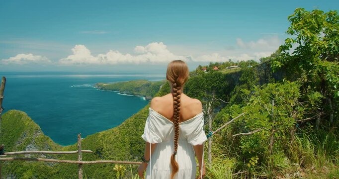 Young woman overlooks the lush green coastline of Nusa Penida island Bali