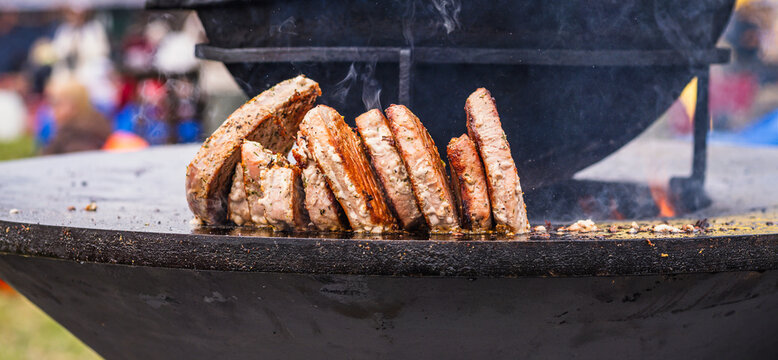 Meat patties grilling on a round metal hot plate. Cook preparing food outdoors over fire. Culinary process of searing beef cutlets for lunch or dinner barbecue.