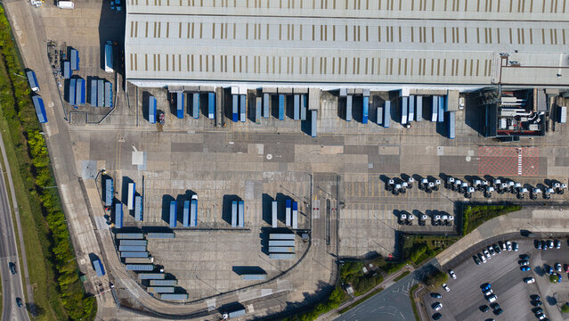 Aerial view of a large industrial warehouse with numerous loading docks, blue semi-trailers, and parked trucks in a distribution center Goole, England, United Kingdom.