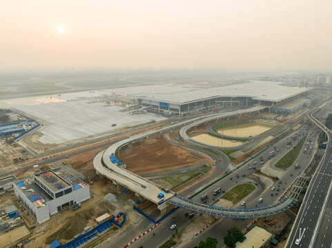 Aerial view of the Hazrat Shahjalal International Airport Terminal 3 under construction with elevated ramps and surrounding traffic under a hazy sky in Dhaka, Dhaka Division, Bangladesh.