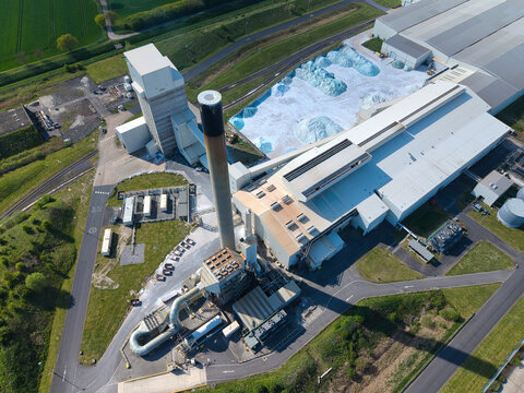 Aerial view of an industrial glass manufacturing facility with a tall chimney stack and large piles of blue glass cullet Goole, England, United Kingdom.