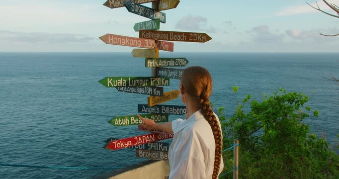 Woman traveler points to Kuala Lumpur on wooden directional signpost at Nusa Penida Bali coastal lookout