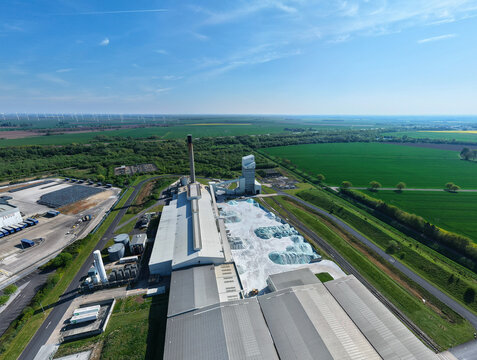Aerial view of the Industrial Glass Manufacturing Facility featuring a tall chimney and raw material storage piles surrounded by green fields in Goole, England, United Kingdom.
