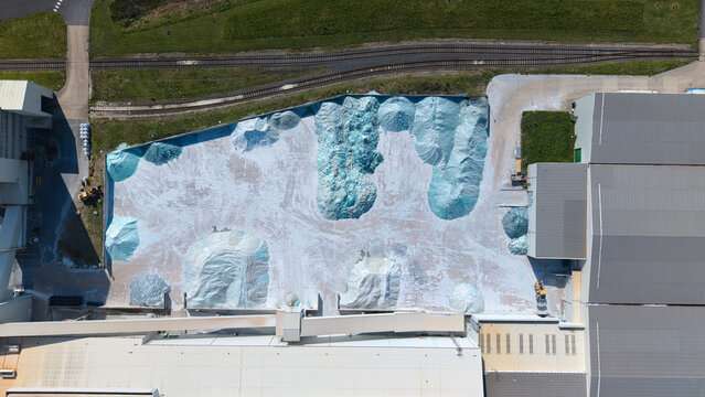 Aerial view of an industrial glass manufacturing facility with large piles of recycled glass cullet and railway tracks in Goole, England, United Kingdom.