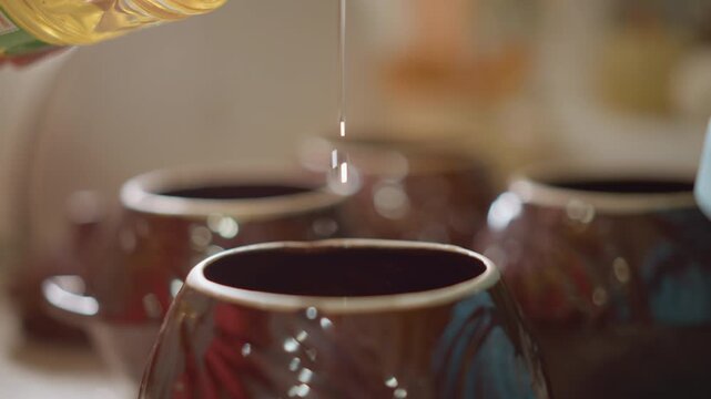 Oil gently falls into gleaming ceramic vessel. Close examination of oil flowing into shiny container. Detailed image capturing oil gradually seeping into reflective glossy ceramic dish