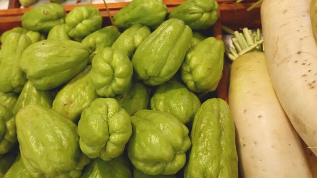 Close up camera panning video shows fresh chayote and daikon radish in supermarket produce section.