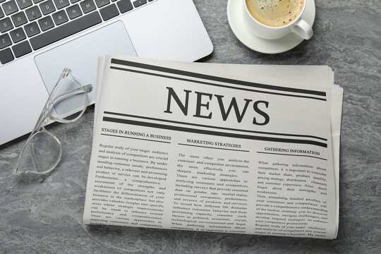 Newspaper, laptop, coffee and glasses on grey desk, flat lay