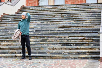 Man stands on stone steps, adjusting his beanie © Iurii Gagarin