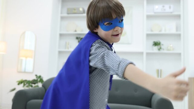 Little boy in superhero costume pretending to fly at home. Camera moving forward and backwards