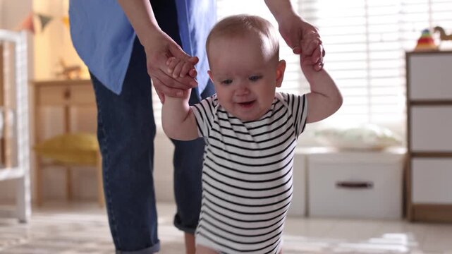 First steps. Mother supporting daughter while she learning to walk at home, closeup