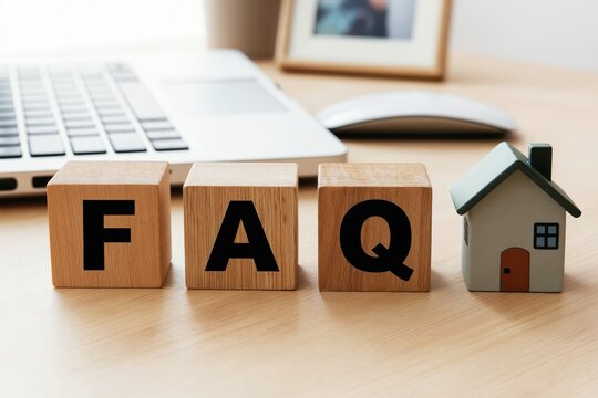 Wooden blocks with letters F A Q stand next to a small house model on a desk. Laptop and mouse are in background. Commonly asked questions about buying or selling a home.