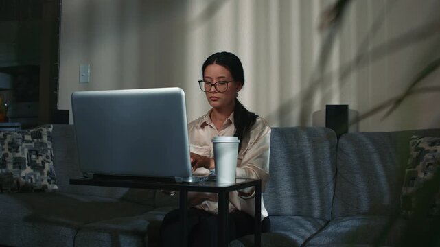 Remote work at home daytime woman on laptop behind plant leaves showing comfortable home atmosphere and productive workflow