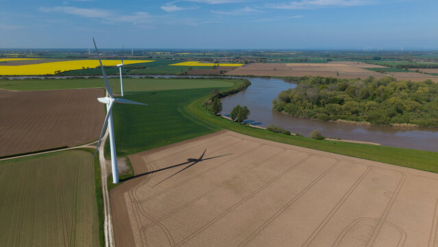 Aerial view of Airmyn Wind Farm turbines standing in agricultural fields beside a winding river under a clear blue sky Airmyn, England, United Kingdom.