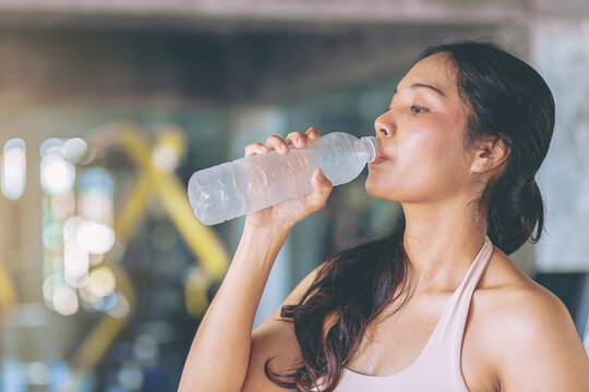 Tired runner woman with a bottle of electrolyte drink freshness after training workout at fitness gym
