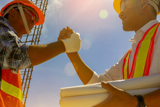 Architect and engineer construction workers shaking hands while working at outdoors construction site. Building construction collaboration concept. Low angle view