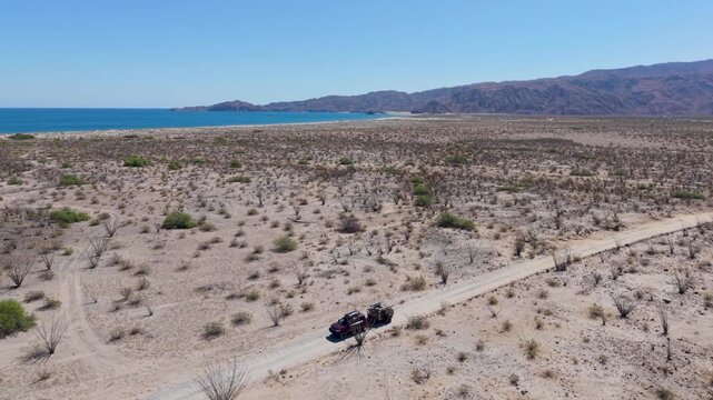 An SUV tows a teardrop camper on dirt roads in Baja California with ocean views during a camping trip in Mexico.