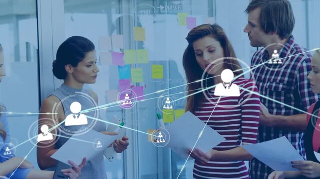 Team moving sticky notes and tapping tablet, creating animated icon network over glass for business