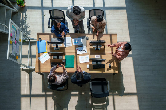 Business team meeting office collaboration strategy marketing model ai planning fuels success as adult coworker applaud around desk with computer overhead view in daylight modern workspace