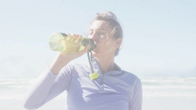 Woman lifting lime bottle to mouth and hydrating at beach, animating hydration ring on bottle