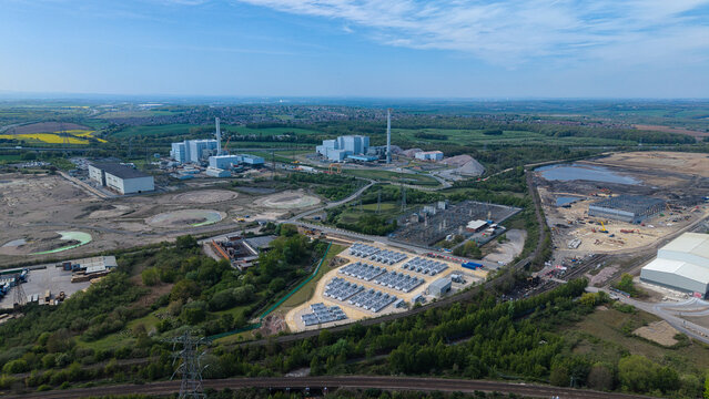 Aerial view of Battery Energy Storage Systems and industrial facilities near a power station with green fields and a blue sky in Knottingley, England, United Kingdom.