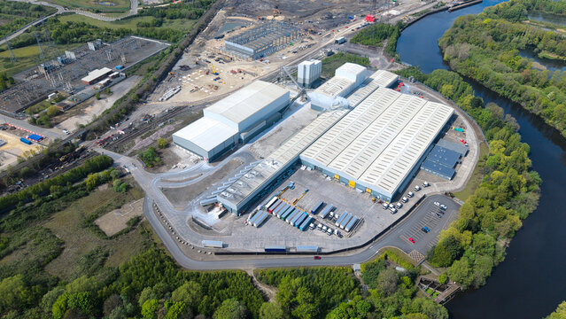 Aerial view of the Ferrybridge industrial complex with large warehouses, parked trucks, and the River Aire in Knottingley, England, United Kingdom.