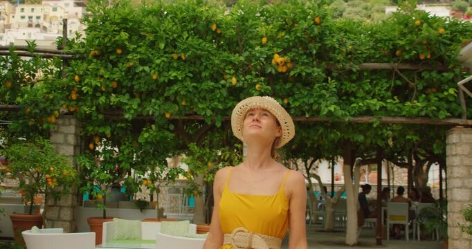 Young woman in summer dress exploring sunny lemon garden cafe in coastal town on Capri Island Italy
