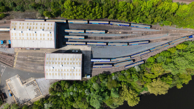 Aerial view of the Ferrybridge railway depot with blue trains parked on tracks next to industrial buildings and lush green trees in Knottingley, England, United Kingdom.