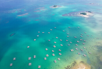 Fototapeta premium Aerial view of dozens of floating net cages (keramba) scattered across the turquoise waters of Tanjung Binga Beach, Belitung, Indonesia, used by traditional fishermen