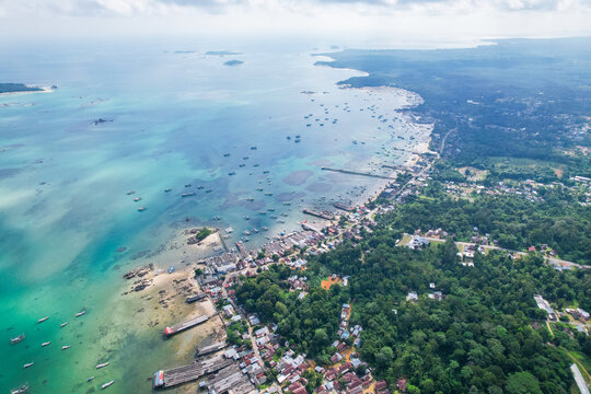 High-angle aerial view of a traditional fishing village in Tanjung Binga, Belitung, Indonesia, featuring coastal houses, fish drying platforms, and boats on turquoise water.