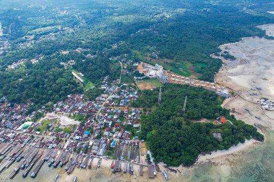High-angle aerial view of a traditional fishing village in Tanjung Binga, Belitung, Indonesia, featuring coastal houses, fish drying platforms, and boats on turquoise water.