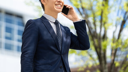 オフィス街でスマートフォンで話す日本人男性ビジネスパーソンのビジネスイメージ, Japanese Businessman Talking on Smartphone in Office District © Trickster*