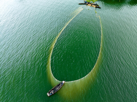 Aerial view of a large fishing net spread in the green water with fishermen in small wooden boats in Rangamati, Chittagong Division, Bangladesh.