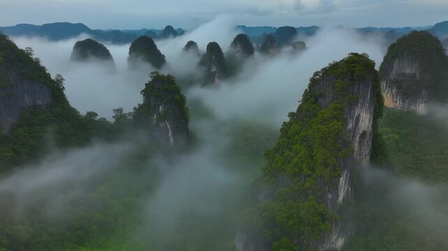 A breathtaking aerial view of lush, green limestone peaks emerging through a thick layer of ethereal clouds in a serene, tropical mountain range.