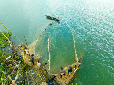 Aerial view of fishermen on wooden boats pulling a large circular fishing net from the green water near a bamboo structure Rangamati, Chittagong Division, Bangladesh.