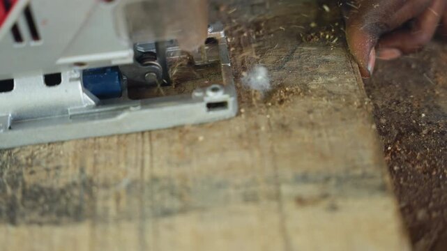 Closeup jigsaw cutting reclaimed wood, steady hand guiding blade along marked line, coarse sawdust and shavings scattering across weathered pallet plank, rustic bench backdrop, measured artisan