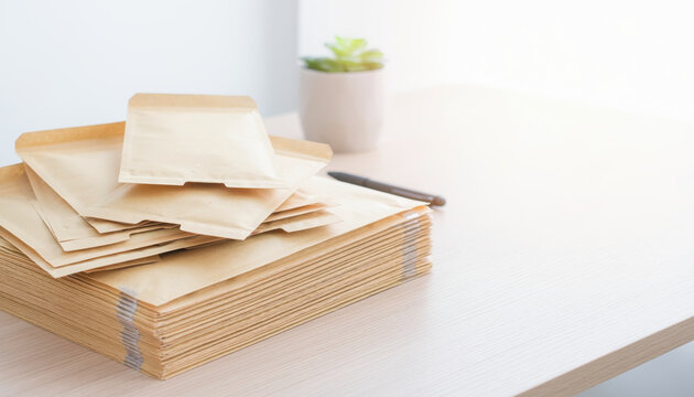 Recycled paper mailer shipping envelope paper mailer packaging parcel stack on desk in bright office, minimalist workspace mood