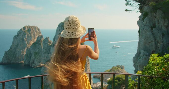 Woman photographs Capri Faraglioni cliffs and summer sea from a scenic viewpoint