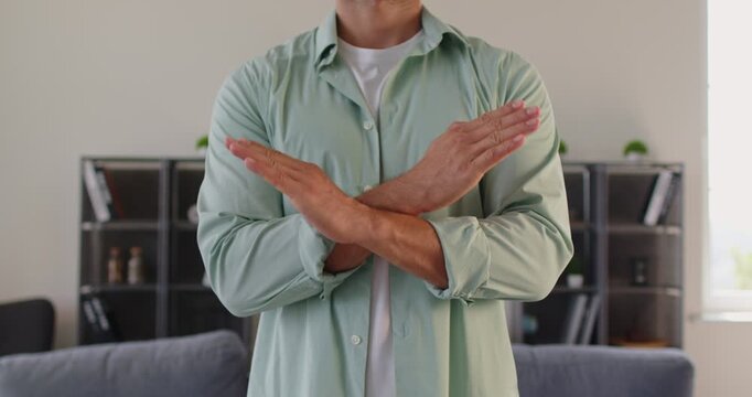 Torso view of man crossing arms into a cross sign, a firm gesture that communicates rejection and stop at home bu hands. He marks boundary to refuse and deny. Clear warning signal in nonverbal form.