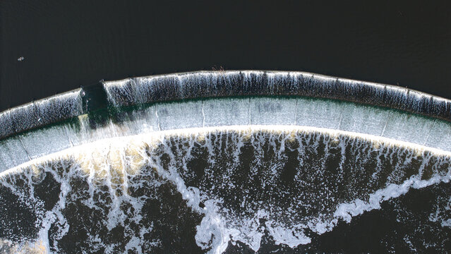 Aerial view of Knottingley Weir and Hydroelectric Power Plant with cascading water creating white foam on the dark river surface in Knottingley, England, United Kingdom.