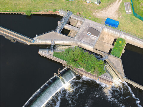 Aerial view of Knottingley Weir and Hydroelectric Power Plant with rushing water over the dam and concrete infrastructure surrounded by green banks Knottingley, England, United Kingdom.