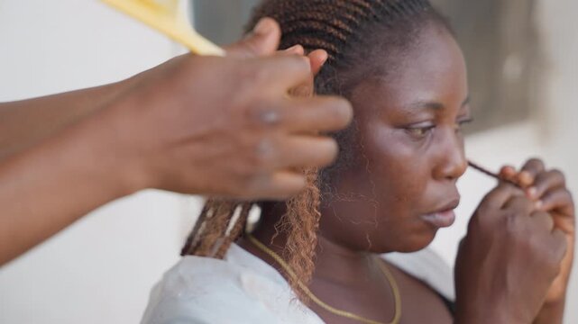 Closeup hair braiding black woman, stylist hands using comb, focused client expression, textured braid strands, warm skin tones, salon setting, clientstylist interaction, cultural hairstyle practice,
