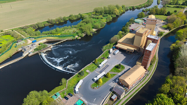 Aerial view of Knottingley Weir and Hydroelectric Power Plant on the River Aire with industrial buildings and lush green trees in Knottingley, England, United Kingdom.